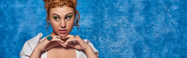 young redhead plus size model with hands near chin looking away on blue backdrop, horizontal banner - Photo, Image