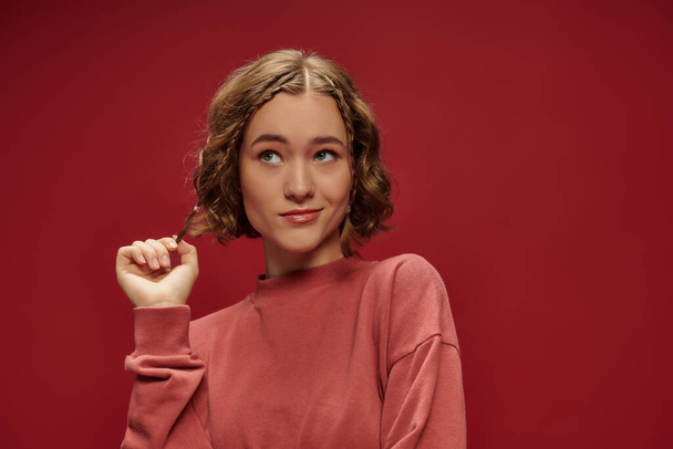 portrait of young pensive woman with short wavy hair and braids looking away on red background - Photo, Image