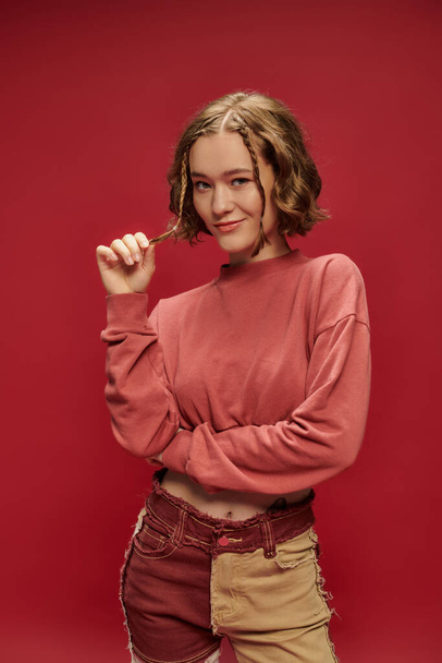 Личный стиль, симпатичная женщина в лоскутных штанах с длинным рукавом, жестикулирующая на красном - Фото, изображение