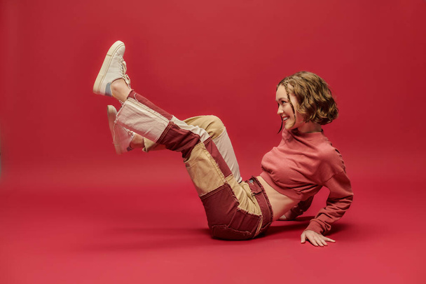 itseilmaisua, iloinen nainen tilkkutäkki housut ja rajattu pitkähihainen istuu punaisella taustalla - Valokuva, kuva