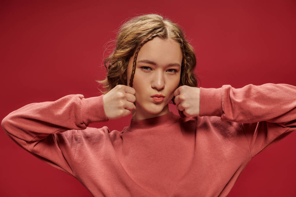 cute gen z girl with short hair and braids posing with clenched fists and looking at camera on red - Photo, Image