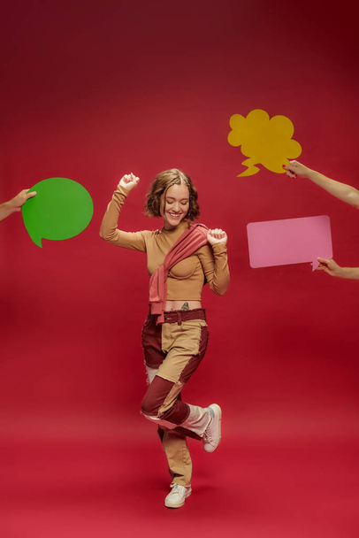 happy woman in patchwork pants and jumper over long sleeve dancing near people with speech bubbles - Photo, Image