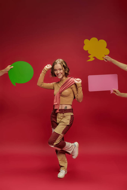 femme joyeuse en patchwork pantalon et pull sur manches longues dansant près des gens avec des bulles de parole - Photo, image