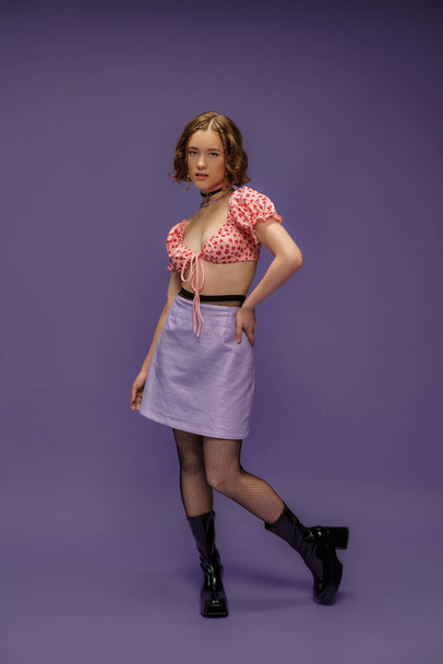 νεαρή γυναίκα σε crop top με καρδιές μοτίβο και φούστα που ποζάρουν με το χέρι στο ισχίο σε μωβ - Φωτογραφία, εικόνα