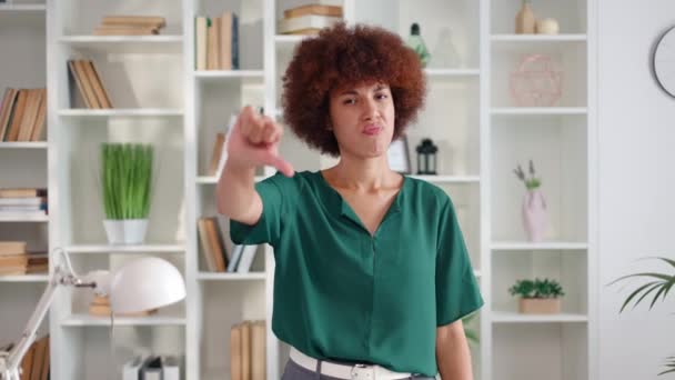 Retrato de jovem insatisfeita de etnia afro-americana vestindo blusa verde mostrando o polegar para baixo gesto. Mulher infeliz expressando emoções negativas com as mãos no escritório. - Filmagem, Vídeo
