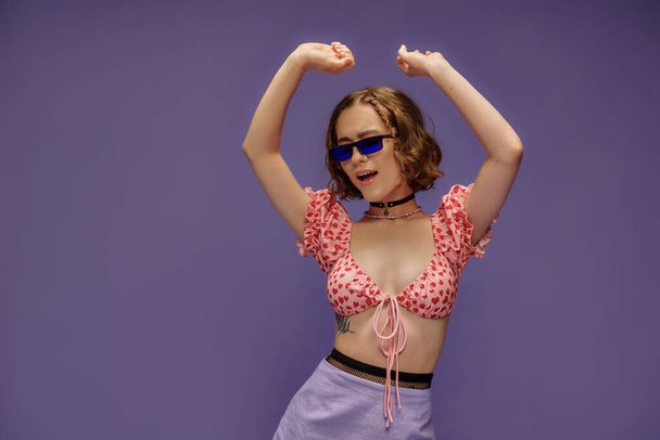 self-expression, young woman in cropped top with hearts and sunglasses singing with raised hands - Photo, Image