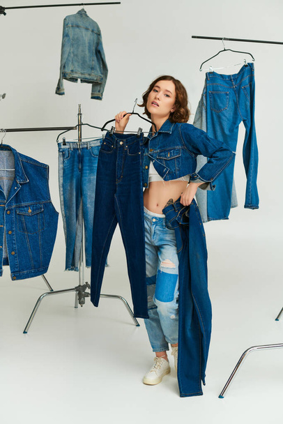 stylisches tätowiertes Model in blauer Kurzjacke mit Jeans zwischen Jeanskleidung auf grauem Hintergrund - Foto, Bild