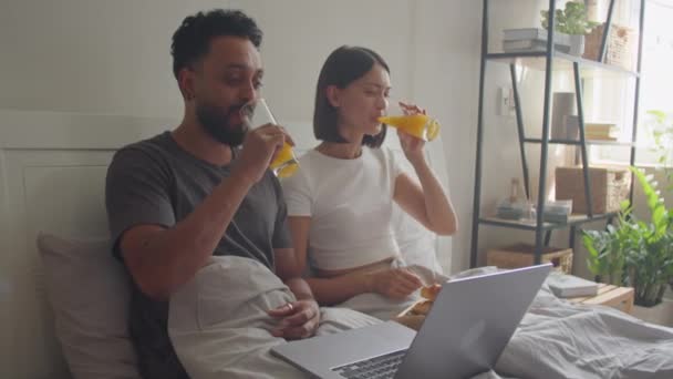 Jong getrouwd stel ontbijten op bed, film kijken op laptop en lachen terwijl het doorbrengen van tijd samen in de ochtend thuis - Video