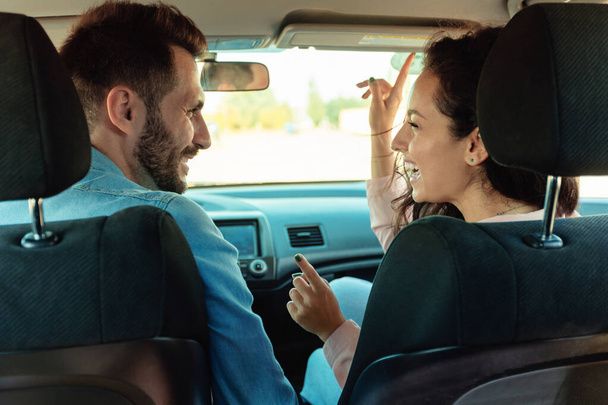 Happy couple sitting in car and singing, enjoying road together, rear view. Driver man and female passenger listening to favorite song in new automobile - Photo, Image