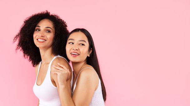 Vielfalt und natürliche Schönheitspflege. Zwei junge multiethnische Frauen posieren isoliert auf rosa Hintergrund, Panorama mit Freiraum, Web-Banner, Platz für Werbung - Foto, Bild