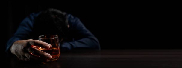 Een man drinkt whisky, een zakenman verlicht stress van zijn werk zittend en whisky drinkend in het kantoor na een zware klus, een dronken man. Alcoholdrinkconcept. - Foto, afbeelding