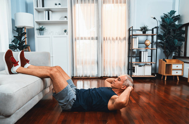 Αθλητικός και ενεργός ηλικιωμένος άνδρας που χρησιμοποιεί έπιπλα για την αποτελεσματική στόχευση των μυών με situp στο σπίτι άσκηση ως έννοια της υγιούς fit τρόπο ζωής του σώματος μετά τη συνταξιοδότηση. Μύγα - Φωτογραφία, εικόνα