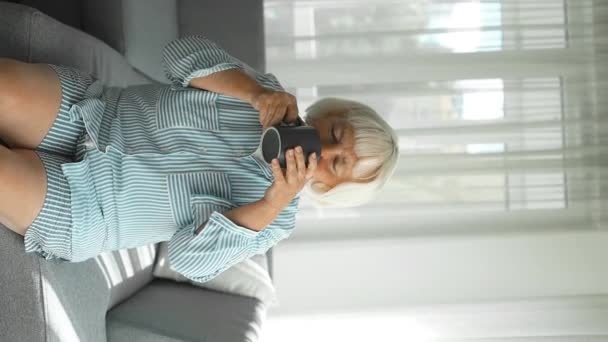 Gelukkig mooie dromerige oude oudere vrouw van middelbare leeftijd zitten op de bank ontspannen thuis hold kopje koffie thee weg te kijken denken dromen genieten van stress gratis rustige stemming welzijn alleen in de woonkamer - Video