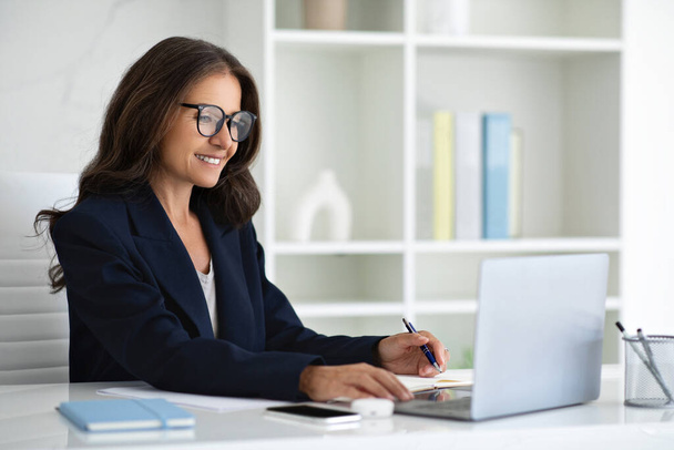 Щаслива зріла жінка в формальному вбранні, окуляри професіонали працюють з офісу на ПК, друкуючи на клавіатурі. Усміхаючись 50-х бізнес-леді використовує ноутбук, надсилає електронні листи, спілкується з клієнтом, копіює простір - Фото, зображення