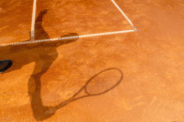 η σκιά ενός τενίστα ή προπονητή σε ανοιχτό πορτοκαλί πηλό γήπεδο του αθλητισμού χτύπημα - Φωτογραφία, εικόνα