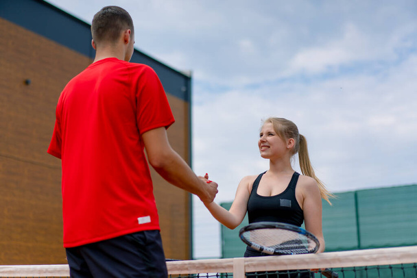 Genç adam ve kadın, tenis maçına başlamadan önce tenis oyuncularına karşı el sıkışıyorlar. - Fotoğraf, Görsel