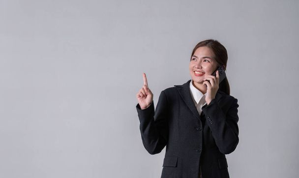 Portrait of a young business woman standing and talking on the phone, pointing, focus according to thoughts.. - Photo, Image