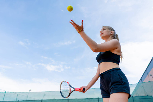 jong meisje beginner tennis speler slaat de bal met een racket op de baan treinen en leert om te slaan dienen sport hobby - Foto, afbeelding