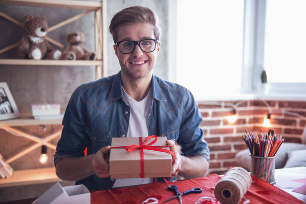 Handsome romantic guy is looking at camera and smiling while holding a handmade present for his couple - Photo, Image