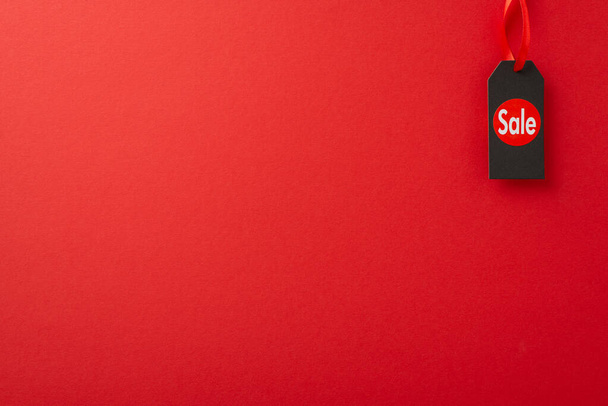 Prudente comprador Viernes Negro inspiración. Fotografía aérea con pegatina de venta en la etiqueta de precio en una superficie roja, proporcionando espacio para contenido promocional - Foto, imagen