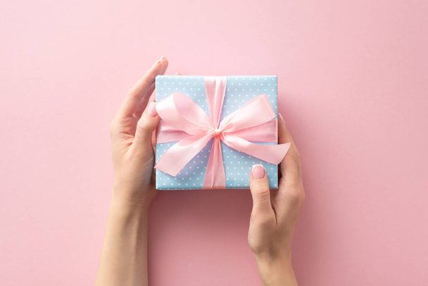 In this first person top view shot, I'm lovingly holding a pastel blue gift box with polka dots and a charming pink ribbon bow. The pastel pink background awaits your text or advertisement - Photo, Image