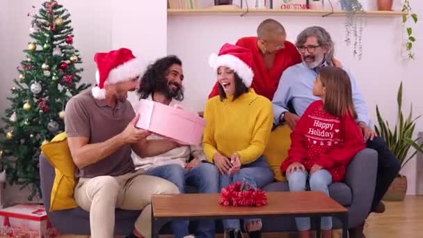 Glückliche Familie feiert Weihnachten zusammen. Schöne junge Frau mit Weihnachtsmannhut eröffnet Geschenk zu Hause an Heiligabend. - Filmmaterial, Video