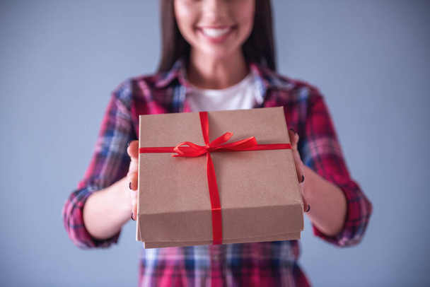 Cropped image of beautiful romantic girl holding a gift box for her couple and smiling, on gray background - Photo, Image