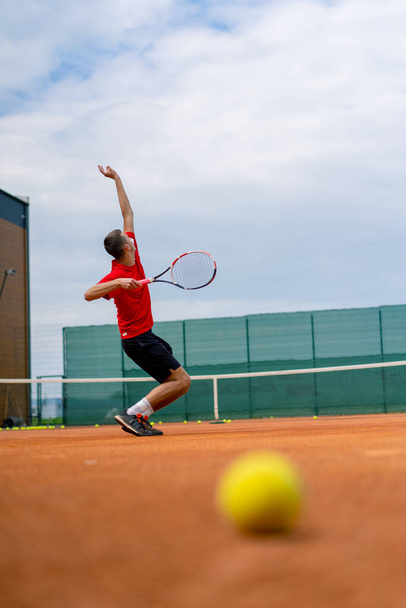 νεαρός επαγγελματίας παίκτης προπονητής σε υπαίθριο γήπεδο τένις προπονήσεις εγκεφαλικά επεισόδια με ρακέτα μπάλα του τένις - Φωτογραφία, εικόνα