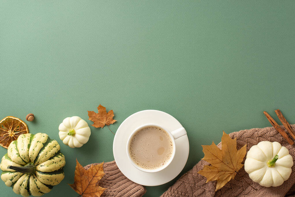 Crisp Podzimní ranní estetika: Z pohledu shora, hnědý pletený svetr, horký šálek kávy, syrové pattypány, žalud, skořicové tyčinky, javorové listy, sušený pomerančový plátek na zeleném pozadí, nabízející prostor pro text - Fotografie, Obrázek