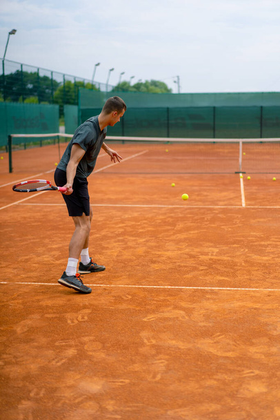 mladý profesionální hráč trenér na venkovním tenisovém kurtu cvičí tahy s raketový tenisový míček - Fotografie, Obrázek
