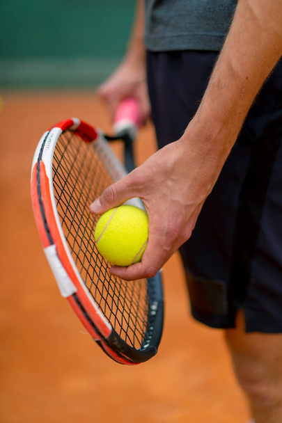 joven entrenador o jugador sosteniendo raqueta de tenis y pelota mientras juega en primer plano de la cancha - Foto, Imagen