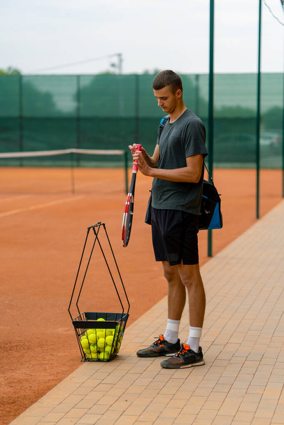 young professional player coach standing on outdoor tennis court before starting game training with racket and basket tennis balls - Photo, Image