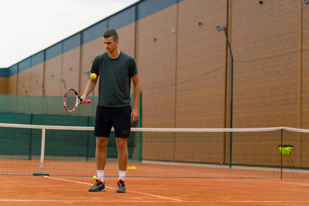 joven entrenador de tenis golpeando la pelota con una raqueta en la cancha de tenis preparándose para el estilo de vida deportivo de competición - Foto, imagen