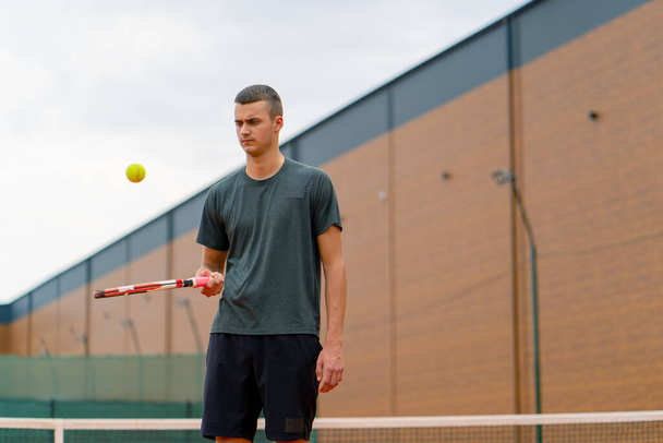 νεαρός προπονητής τενίστας χτυπάει την μπάλα με ρακέτα στο γήπεδο του τένις προετοιμασία για τον αθλητισμό του ανταγωνισμού τρόπο ζωής - Φωτογραφία, εικόνα