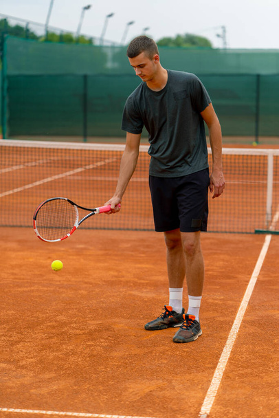 junger Tennisspielertrainer, der auf dem Tennisplatz mit dem Schläger auf den Ball einschlägt und sich auf den Wettkampfsport vorbereitet - Foto, Bild