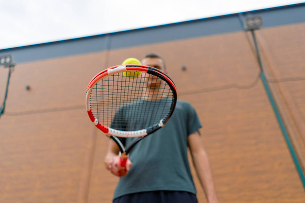 Nahaufnahme junger Tennisspielertrainer, der auf dem Tennisplatz den Ball mit dem Schläger schlägt und sich auf den Wettkampfsport vorbereitet - Foto, Bild