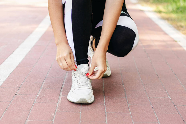 Gros plan de la jeune femme se préparant pour le jogging en plein air tout en lacant ses baskets. Santé et sport concept - Photo, image