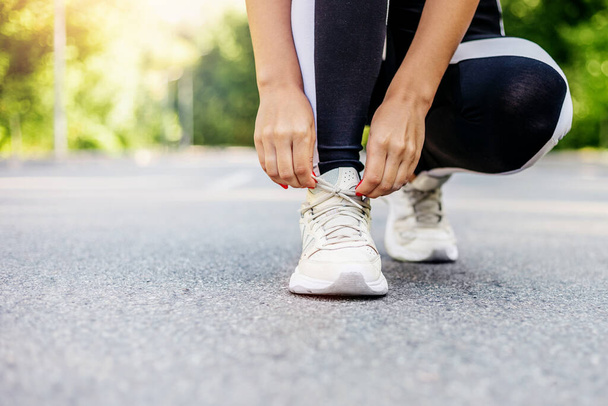Закрыть молодую женщину, готовящуюся к пробежке на свежем воздухе, пока она шнурует кроссовки. Концепция здоровья и спорта - Фото, изображение
