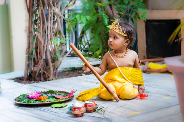 αξιολάτρευτο βρέφος ντυμένο σαν ινδουιστής θεός krishna χαριτωμένη έκφραση προσώπου με φλάουτο στο janmashtami - Φωτογραφία, εικόνα
