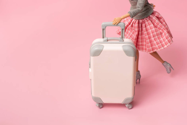 Lalka nosi walizkę na kołach. Podróże, wakacje twórcza minimalistyczna koncepcja. - Zdjęcie, obraz