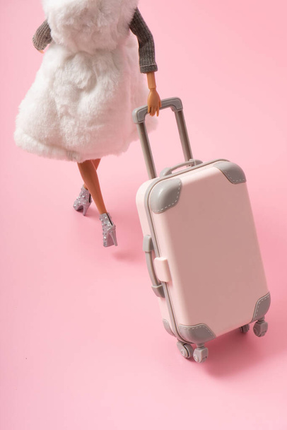 La bambola porta una valigia su ruote. Viaggio, vacanza creativo concetto minimalista. - Foto, immagini