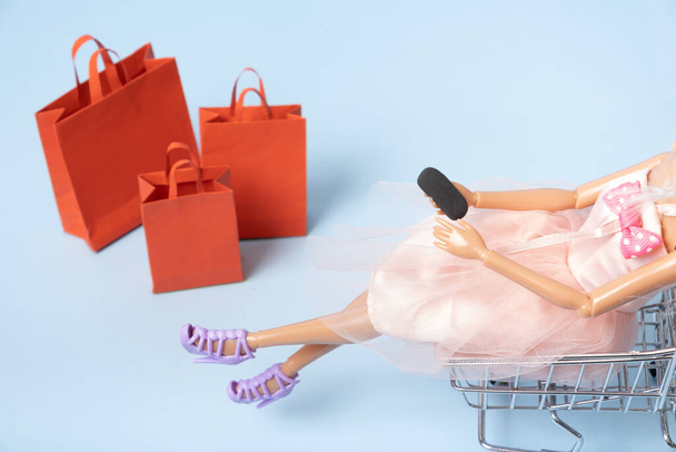 Лялька в кошику супермаркетів зі смартфонами та торговими пакетами зверху. Концепція продажу. - Фото, зображення