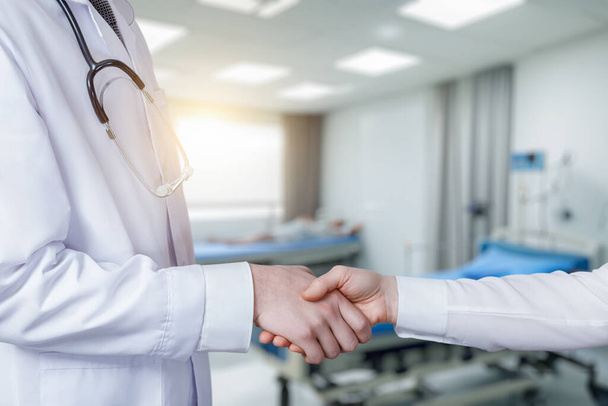 The doctor supports the patient with a handshake on a blurred background. - Photo, Image