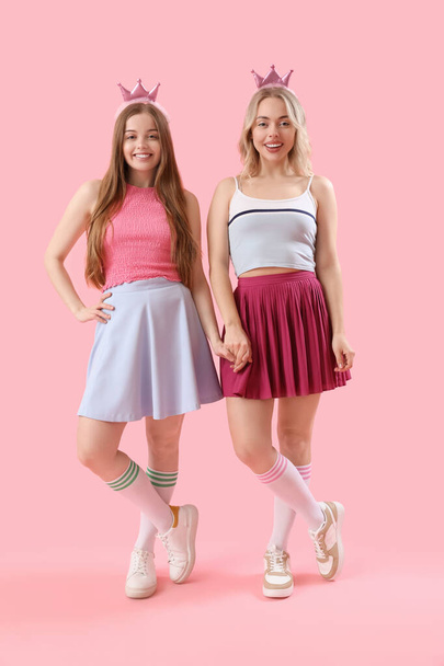 Молоді сестри в коронках тримають руки на рожевому фоні
 - Фото, зображення