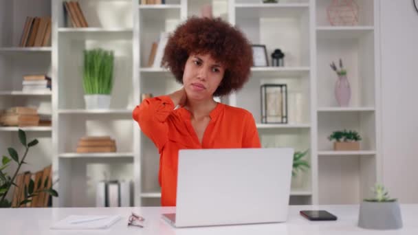 Kimerült multikulturális nő masszírozza a nyakát erős fájdalom miatt hosszú munkaidő után vezeték nélküli laptopon a modern irodában. Üledékes munkavégzésből eredő egészségügyi problémák. - Felvétel, videó