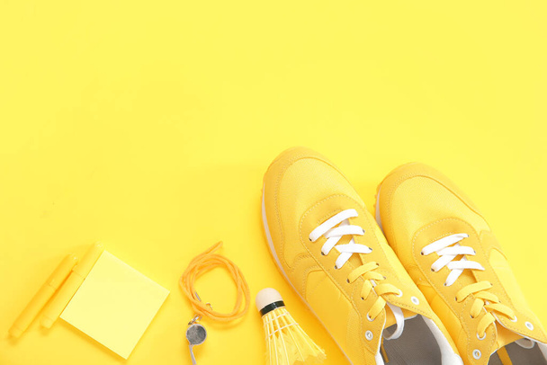 Sneakers with whistle, shuttlecock and stationery on yellow background - Photo, Image