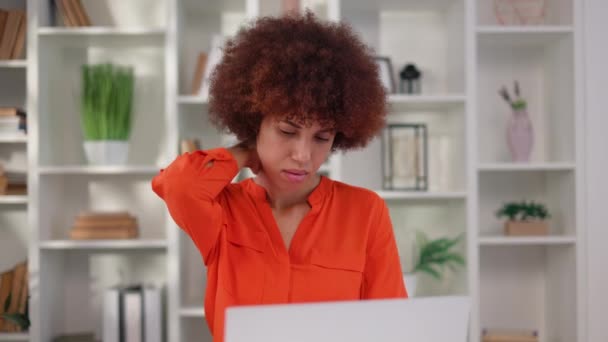 Malaise jeune femme toucher le cou avec la main parce que sentir la douleur après avoir travaillé en ligne sur un ordinateur portable personnel. Femme afro-américaine fatiguée étirant le corps après un emploi de longue date au bureau. - Séquence, vidéo