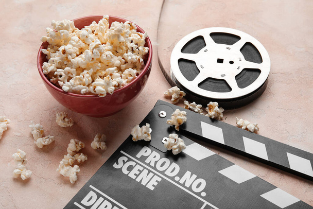 Bowl ízletes popcorn, clapperboard és filmtekercs könnyű háttér - Fotó, kép