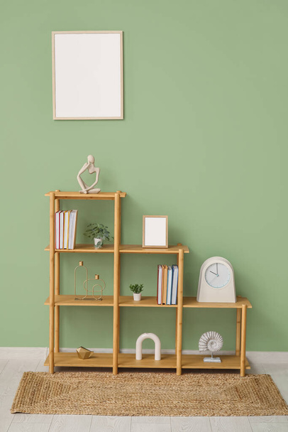 Shelving unit with books, decor and blank frame hanging on green wall in room - Photo, Image
