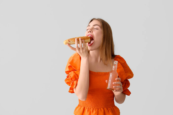 mooie jonge vrouw met smakelijke hotdog en drinken op grijze achtergrond - Foto, afbeelding